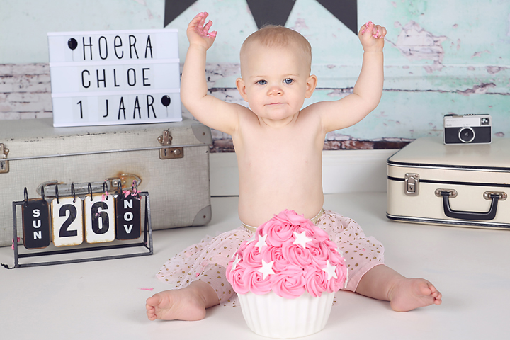 Juichend babymeisje met roze taart bij haar eerste verjaardag, cakesmash