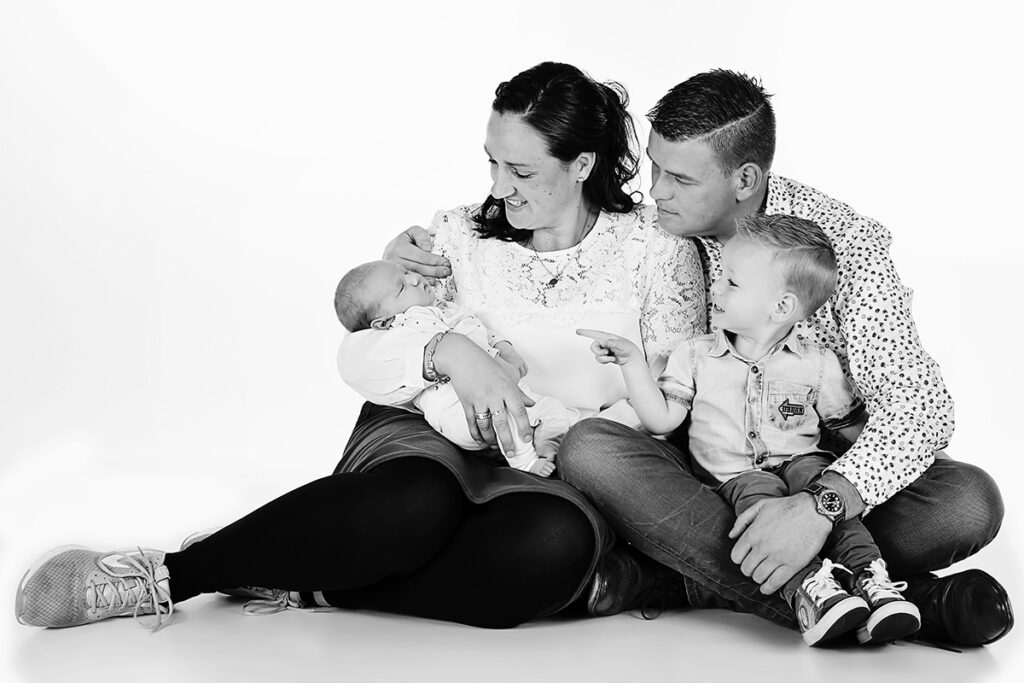 Zwart-witfoto van ouders en grote broer met de newborn op de studiovloer