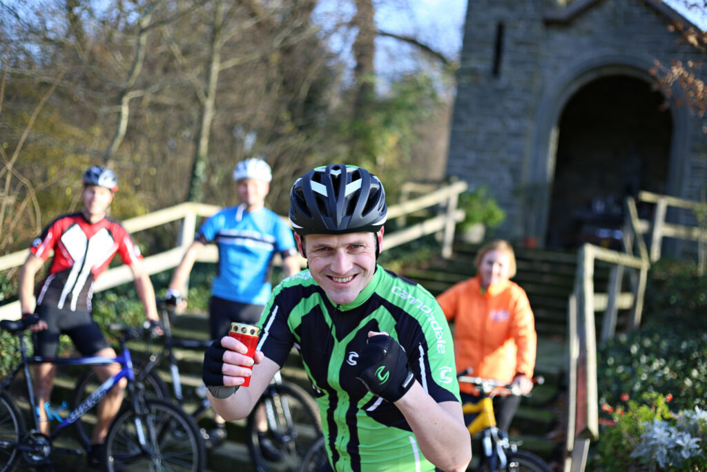 Lachende wielrenner met helm en sportdrank, met andere fietsers op de achtergrond