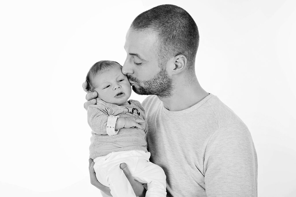 Zwart-witfoto van een vader die zijn pasgeboren baby kust