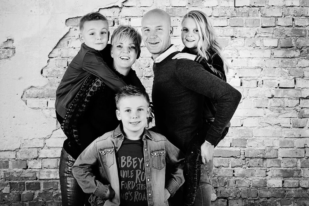 Zwart-witfoto van een gezin voor een witte bakstenen muur, familiefotografie