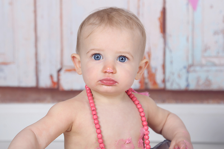 Baby met roze ketting tegen een houten achtergrond, kinderportret