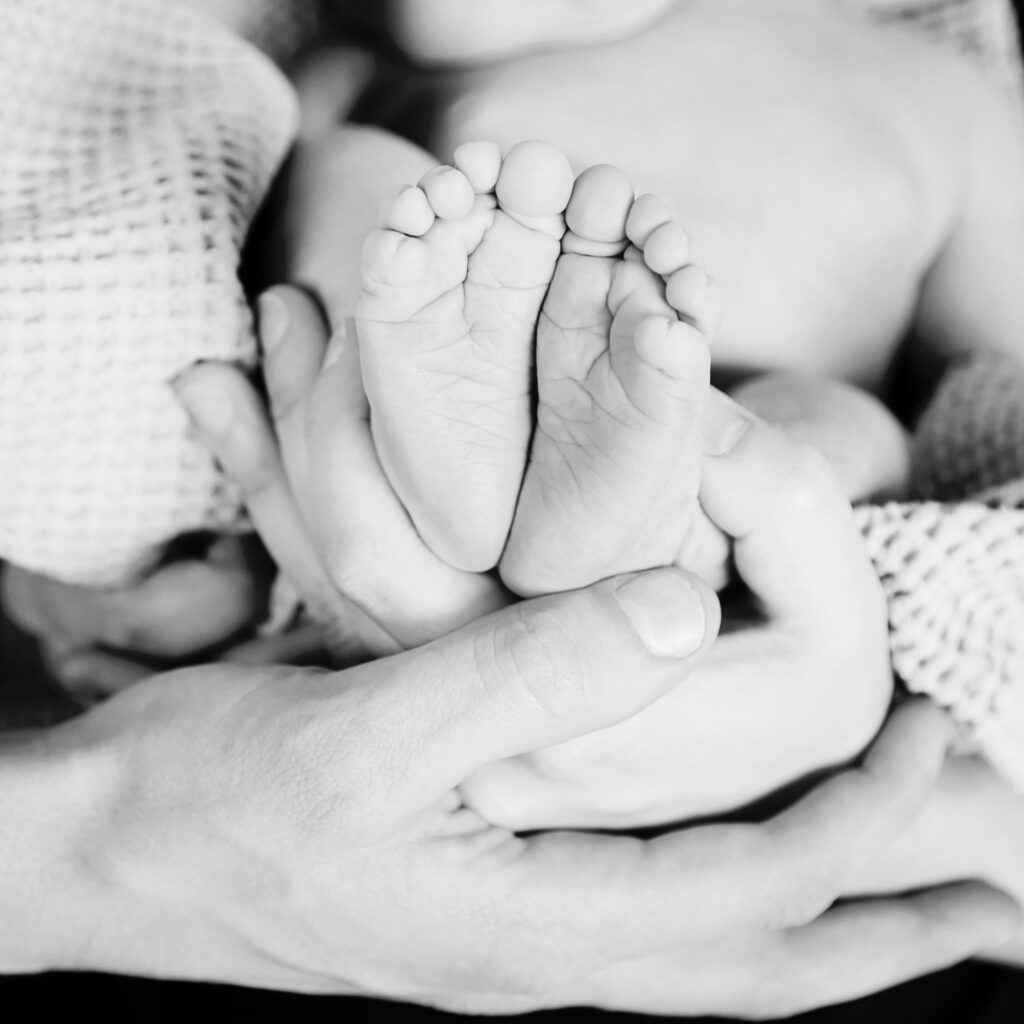 Zwart-witfoto van babyvoetjes in de handen van de ouders