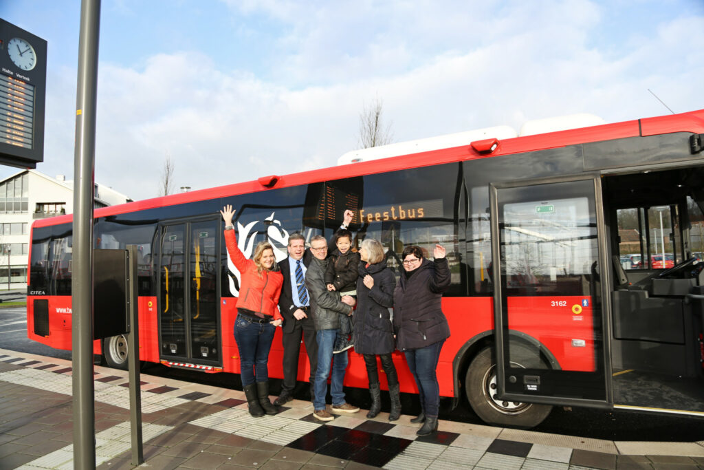 Groep zwaait enthousiast bij een rode Freebus aan een bushalte