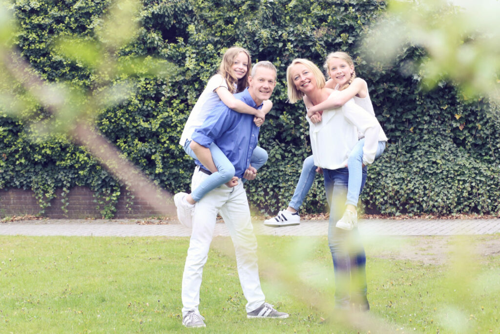 Ouders dragen hun dochters op de rug in een zonnige tuin