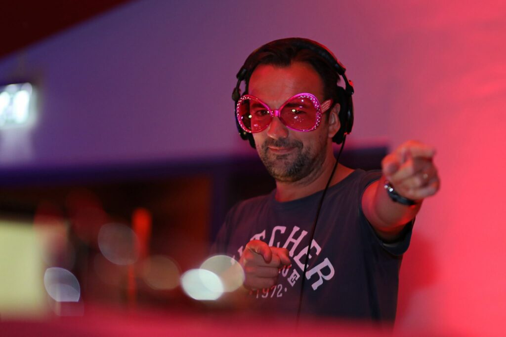 DJ met koptelefoon en roze bril wijst naar het publiek, feestfotografie