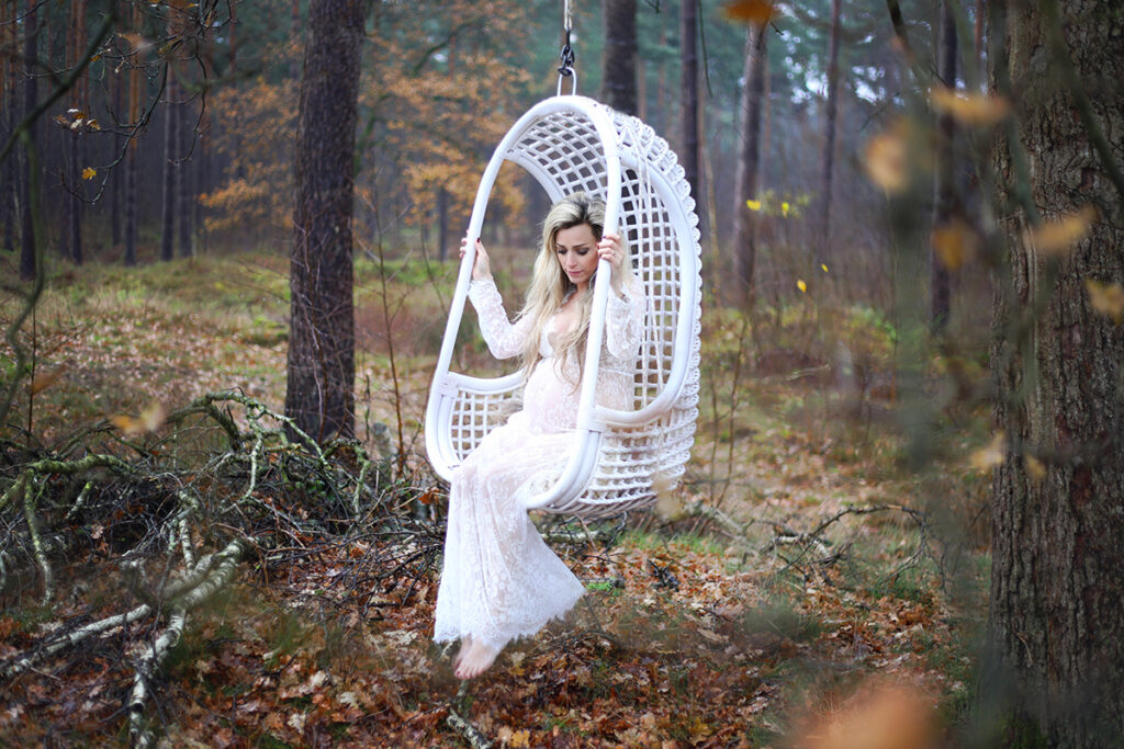 Zwangere vrouw in een witte hangstoel in het bos