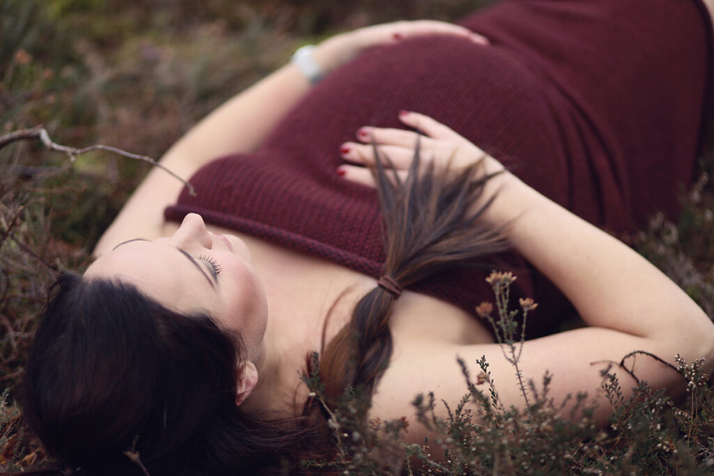 Zwangere vrouw ligt in de heide met hand op haar buik