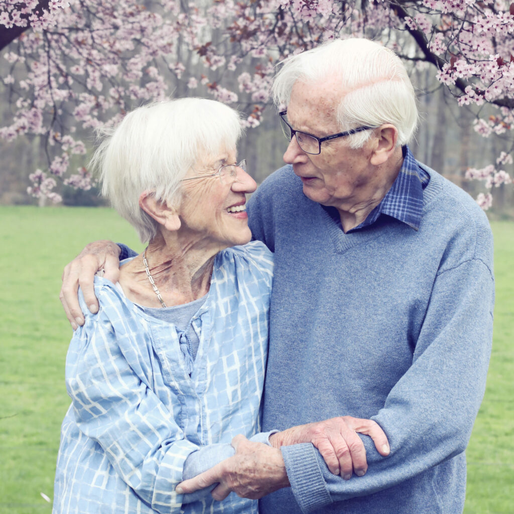 Opa en oma lachen elkaar toe onder een bloesemboom, opa en oma fotografie