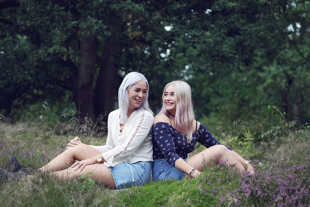Moeder en volwassen dochter zitten samen in het gras, familiefotografie