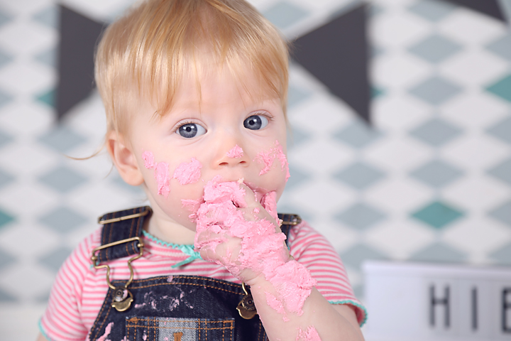 Blonde peuter likt roze taart van zijn handje, cakesmash