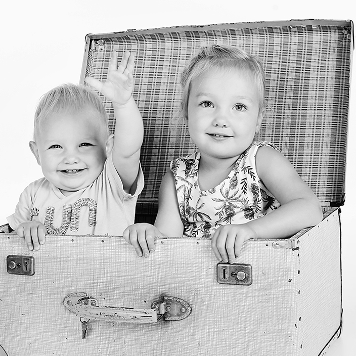 Zwart-witfoto van twee lachende kinderen in een oude koffer