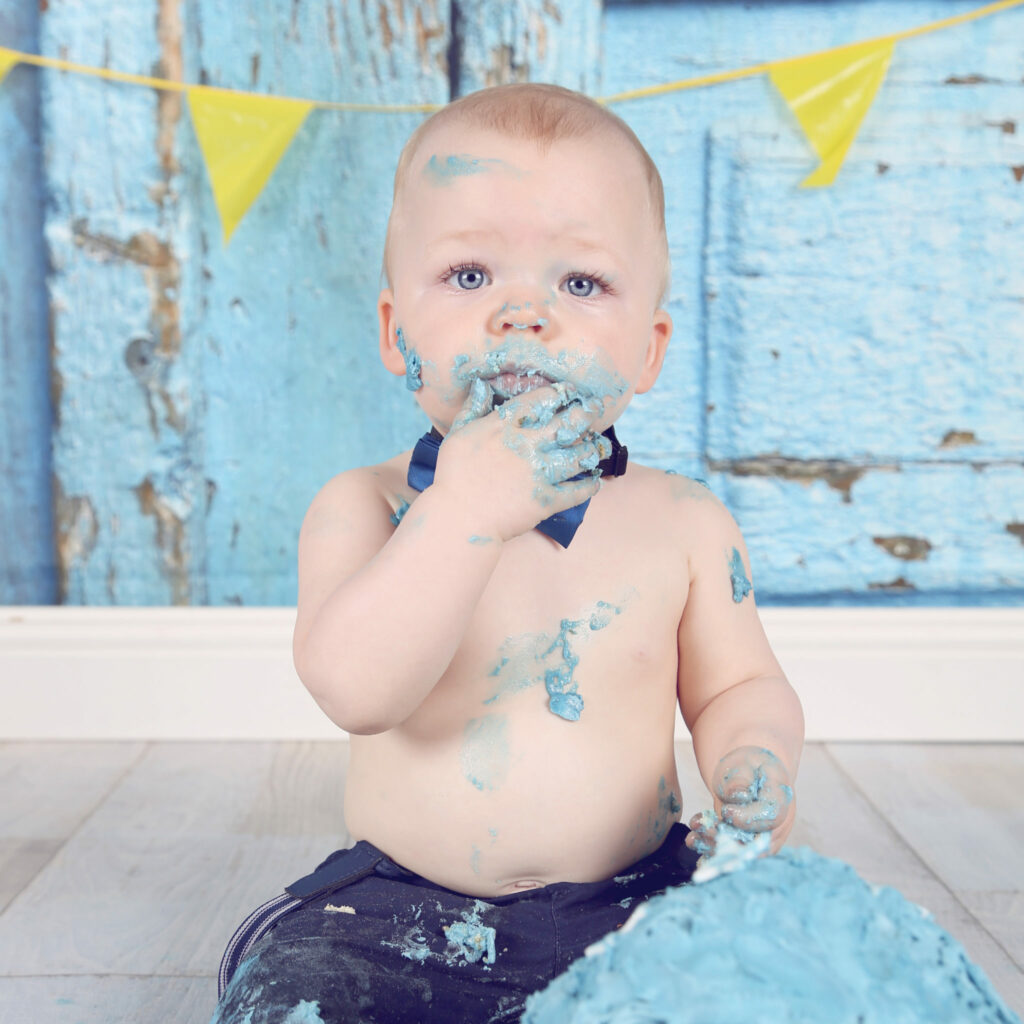 Baby met blauwe taart in zijn gezicht onder gele vlaggetjes, cakesmash