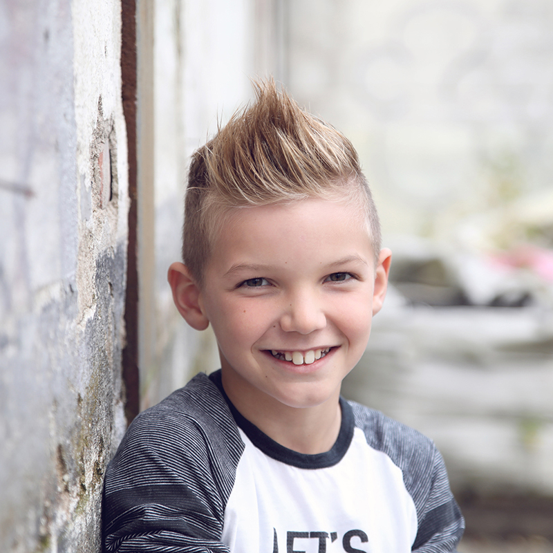 Lachende jongen met hanenkam bij een oude muur, kinderportret