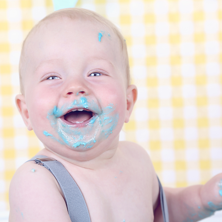 Close-up van een lachende baby met blauwe slagroom, cakesmash