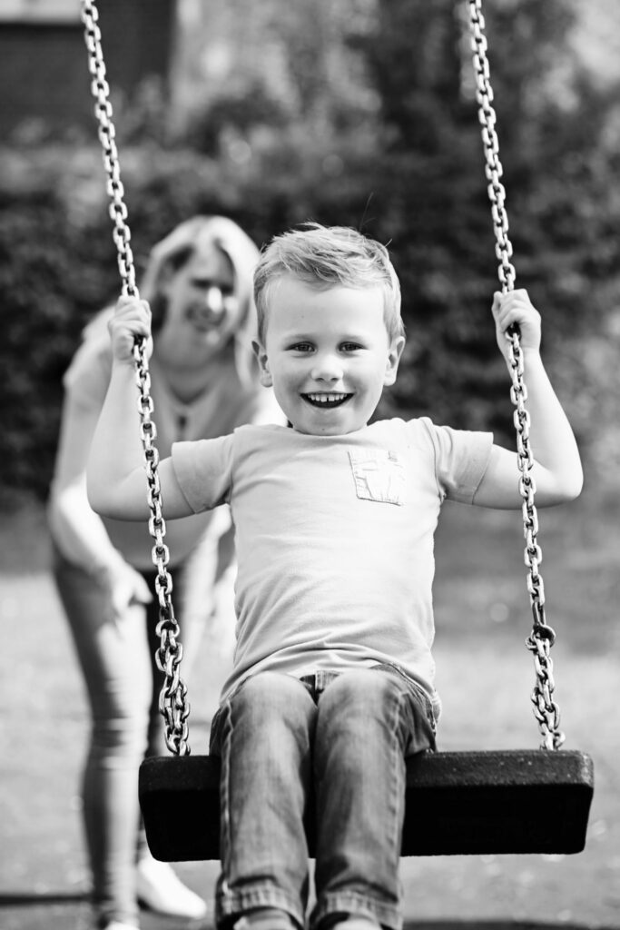 Zwart-witfoto van een lachend jongetje op een schommel, familieshoot