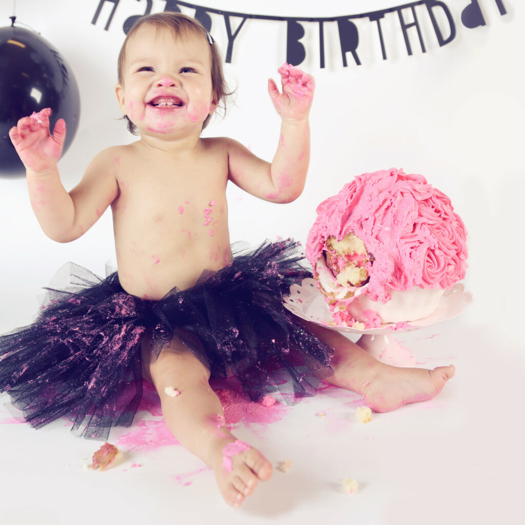 Lachend meisje in paarse tutu met roze taart, eerste verjaardag cakesmash