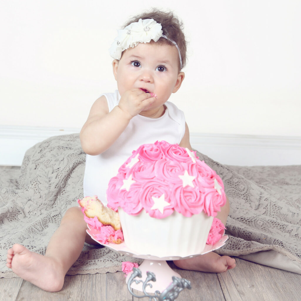 Babymeisje met haarband en roze taart tijdens een cakesmash-fotoshoot