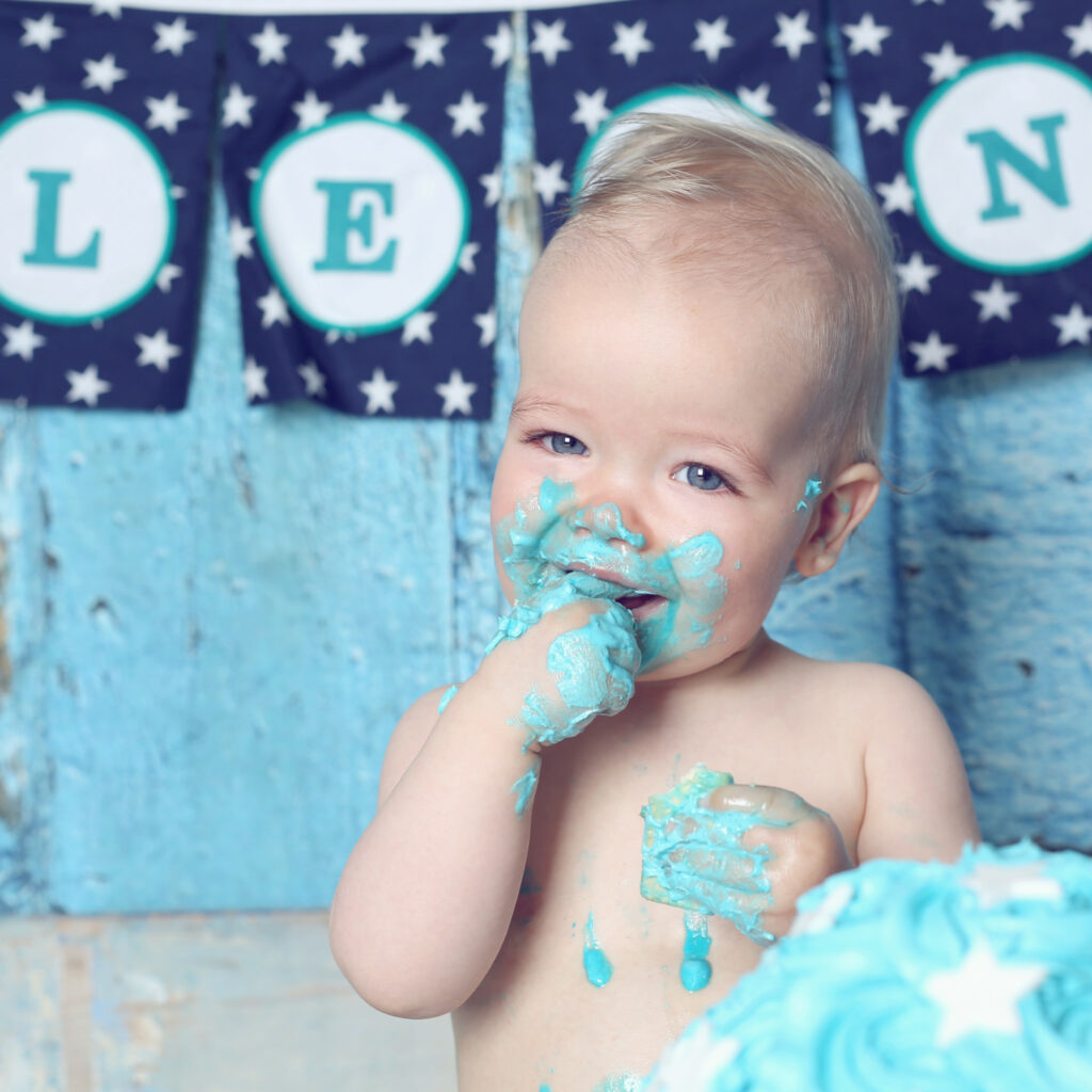 Baby likt blauwe slagroom van zijn vingers bij een cakesmash met naambanner