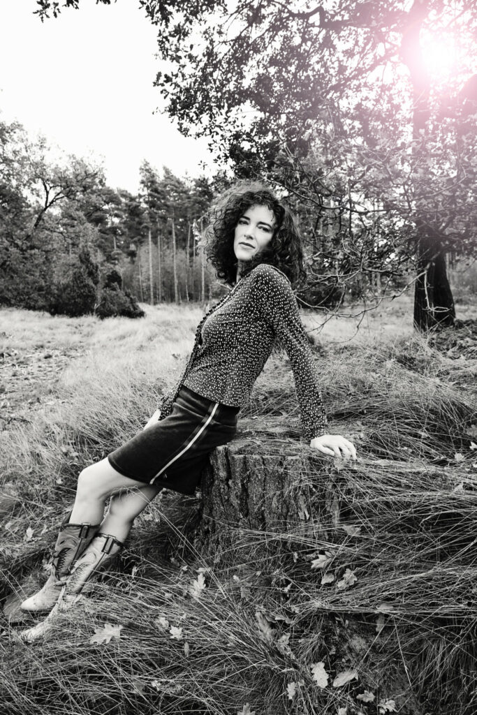 Zwart-witfoto van een vrouw in rok en trui in het gras, fashion shoot buiten
