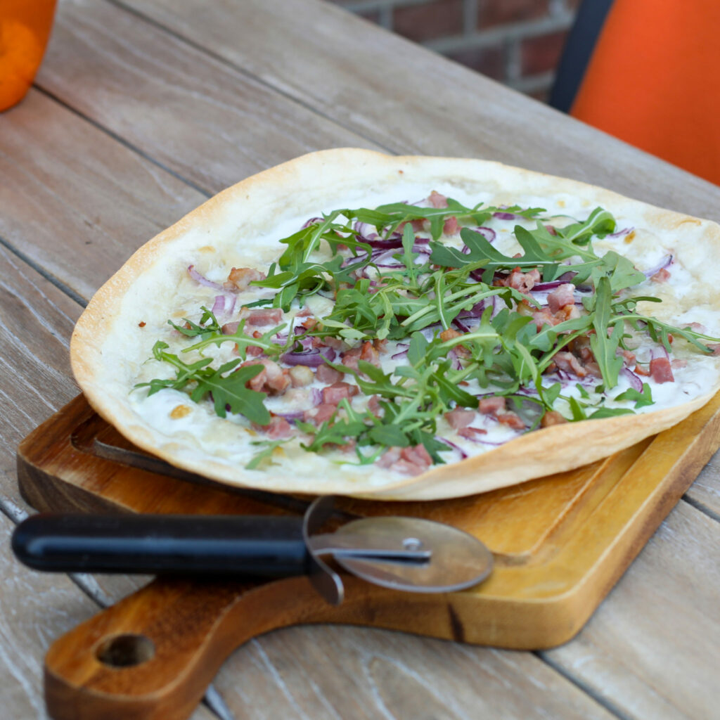 Flammkuchen met rucola op een houten plank met pizzasnijder