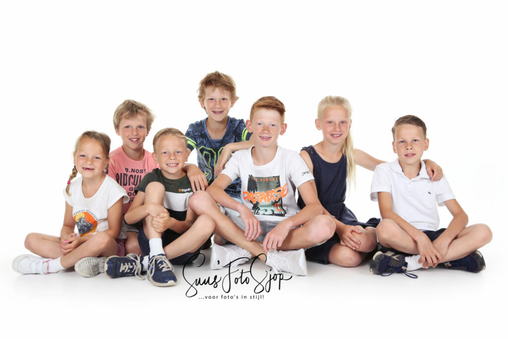 Zes kleinkinderen zitten op een rij in de witte studio