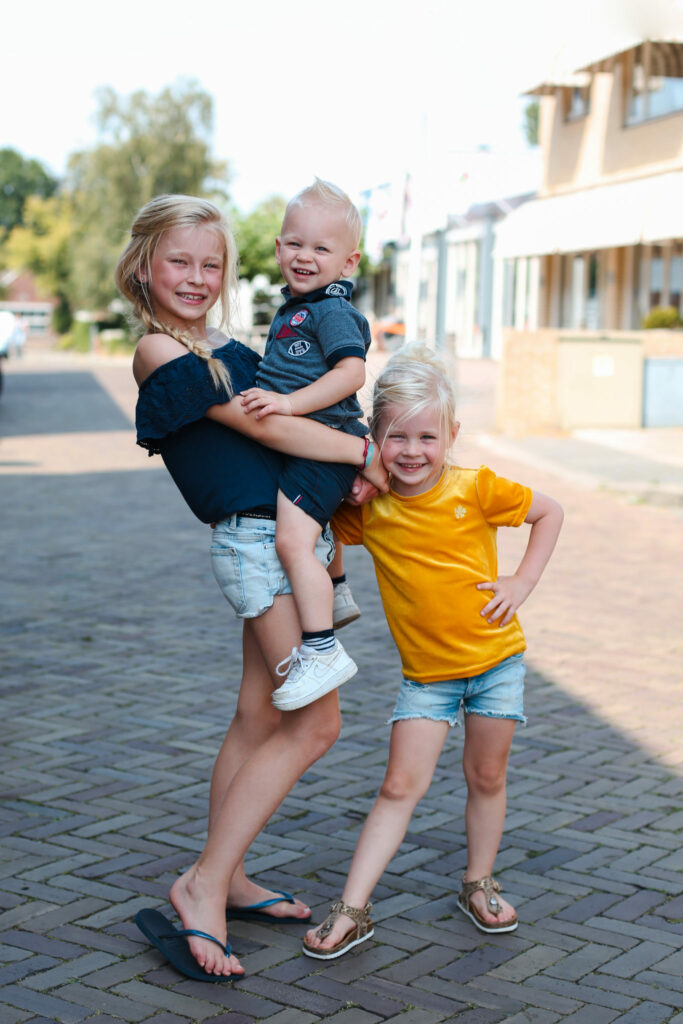 Zusje draagt haar broertje in een straat terwijl een tweede zus lacht