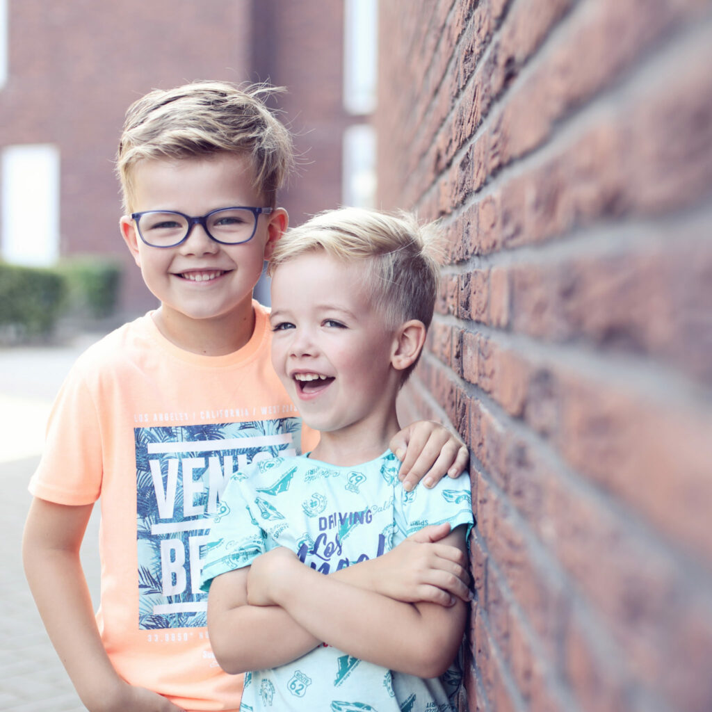 Twee lachende broertjes tegen een bakstenen muur, kinderfotografie