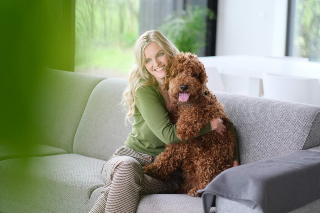 Vrouw knuffelt haar bruine labradoodle op de bank thuis