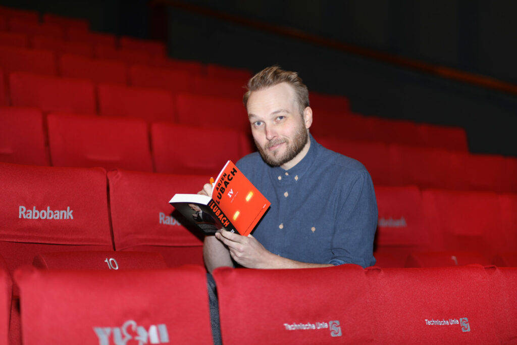 Man leest in een rij rode theaterstoelen, portret in een theater