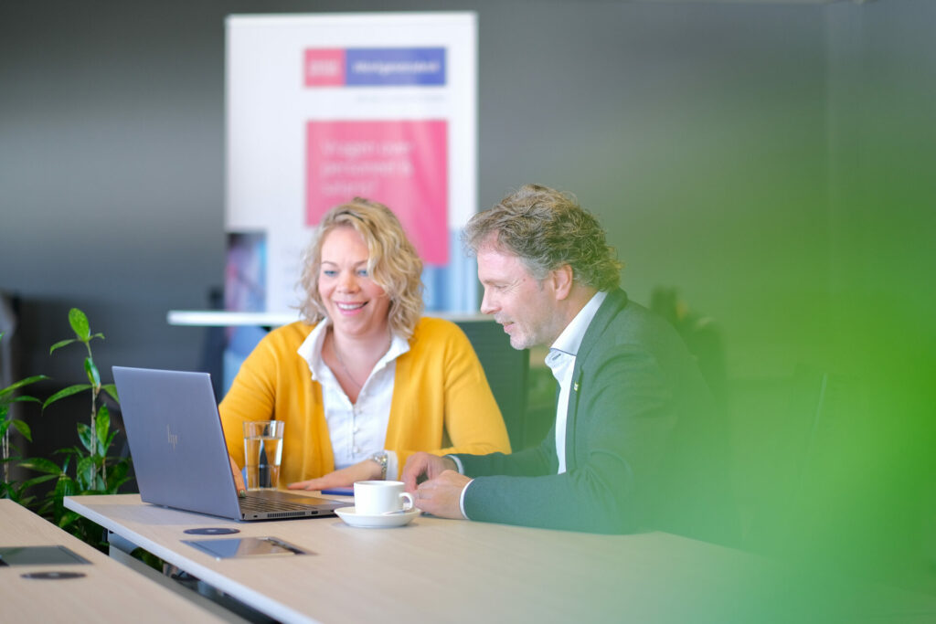 Twee collega's overleggen aan tafel met laptop, zakelijke content