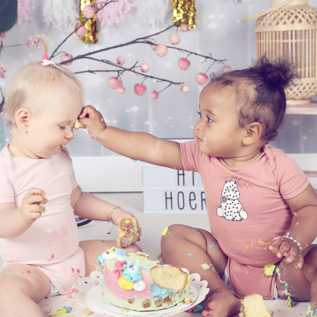Twee babymeisjes delen samen een taart tijdens een cakesmash