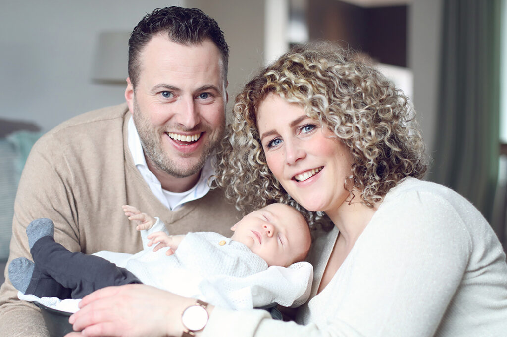 Ouders kijken lachend naar hun pasgeboren baby in de woonkamer