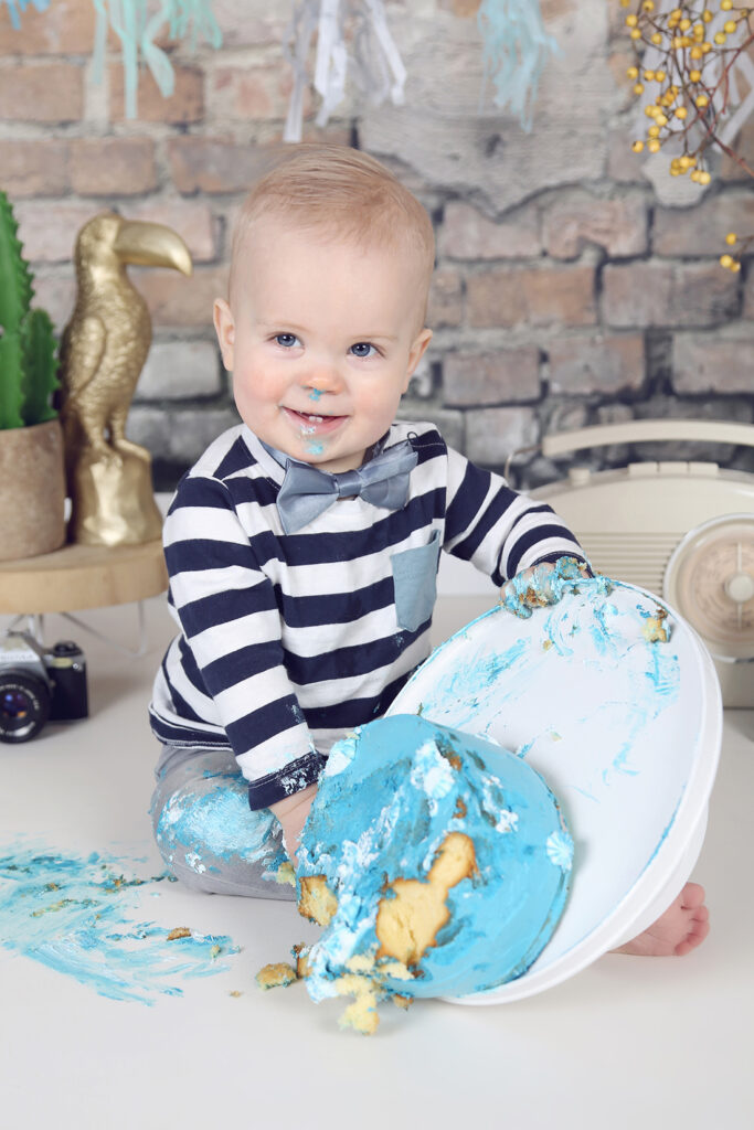 Jongetje in gestreept shirt met blauwe taart voor een stenen muur, cakesmash