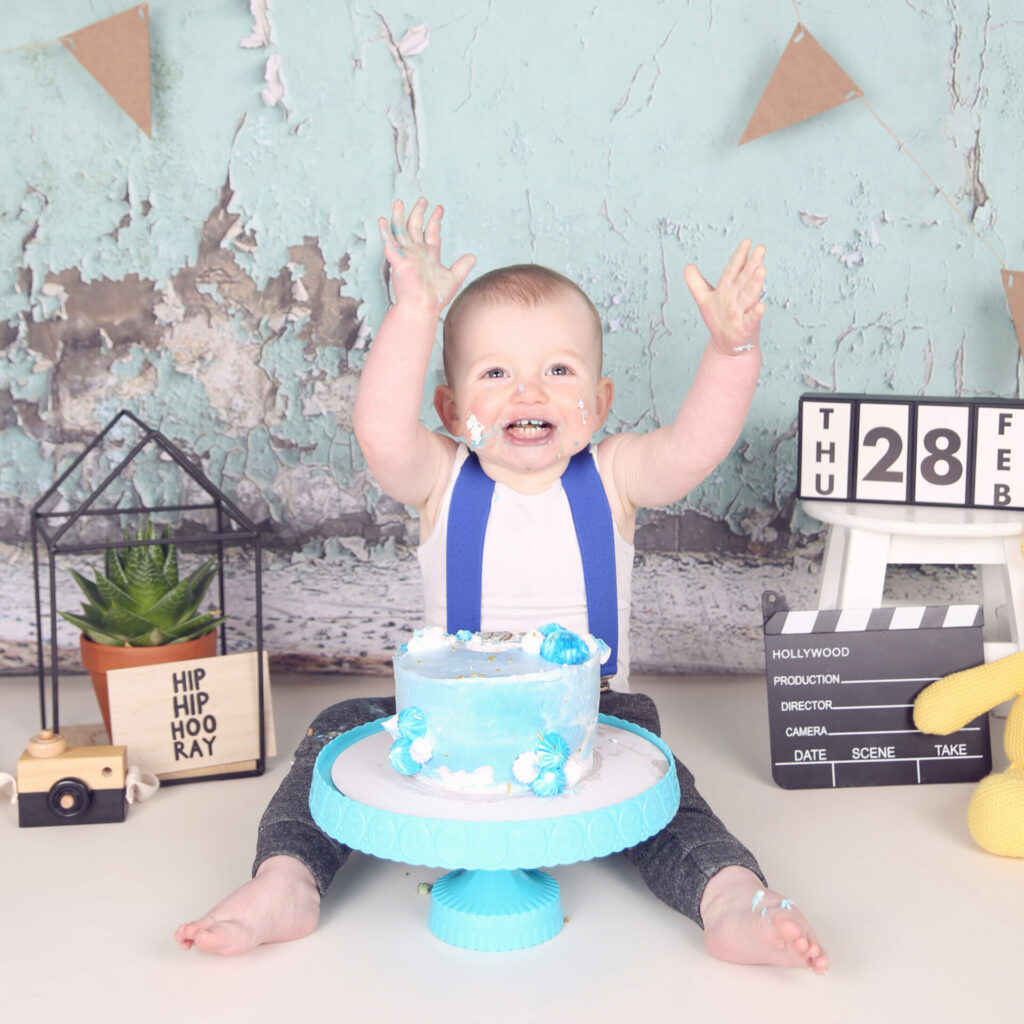 Juichende baby met blauwe taart en bretels bij een cakesmash-fotoshoot