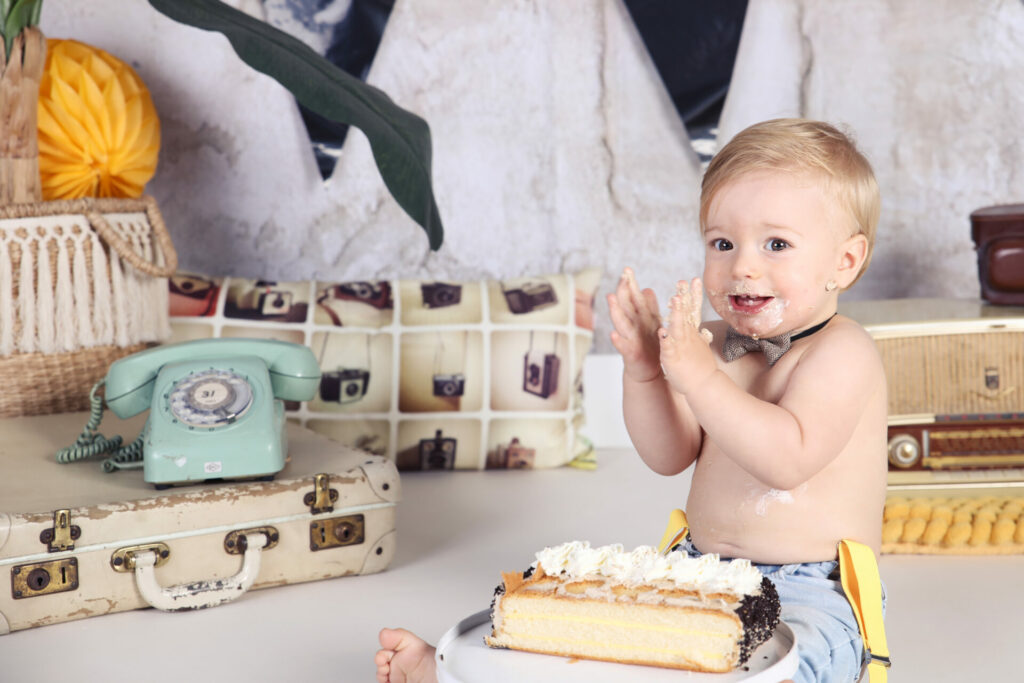 Lachende baby met taart tussen vintage koffers en telefoon, cakesmash