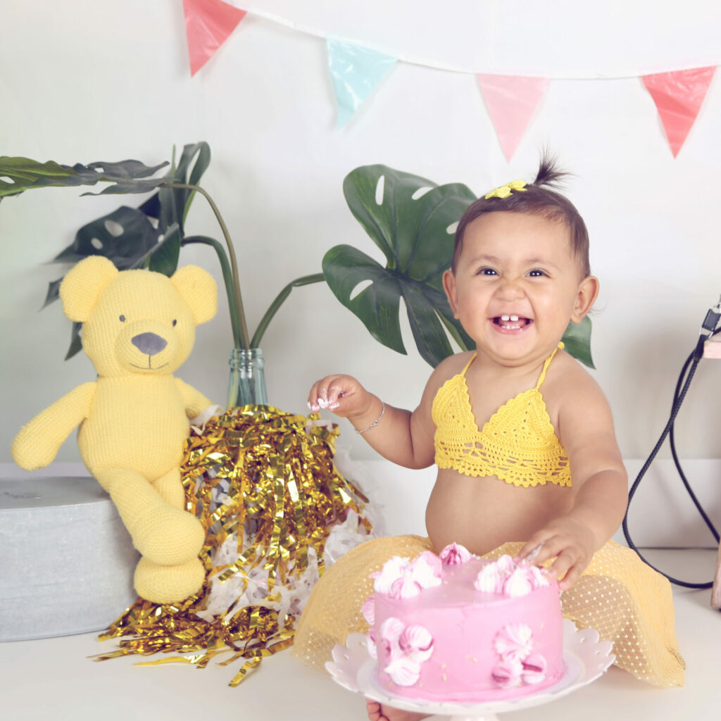 Lachend meisje in geel met roze taart en gele knuffelbeer, cakesmash-fotoshoot