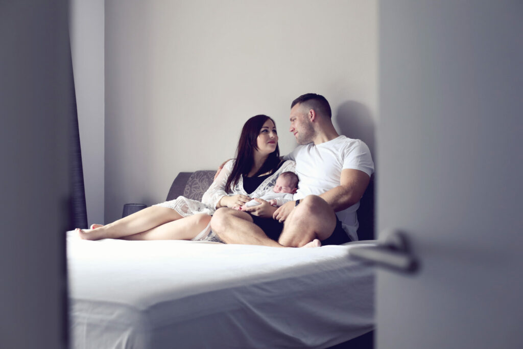 Ouders met hun pasgeboren baby op bed bij hen thuis, lifestyle familieshoot
