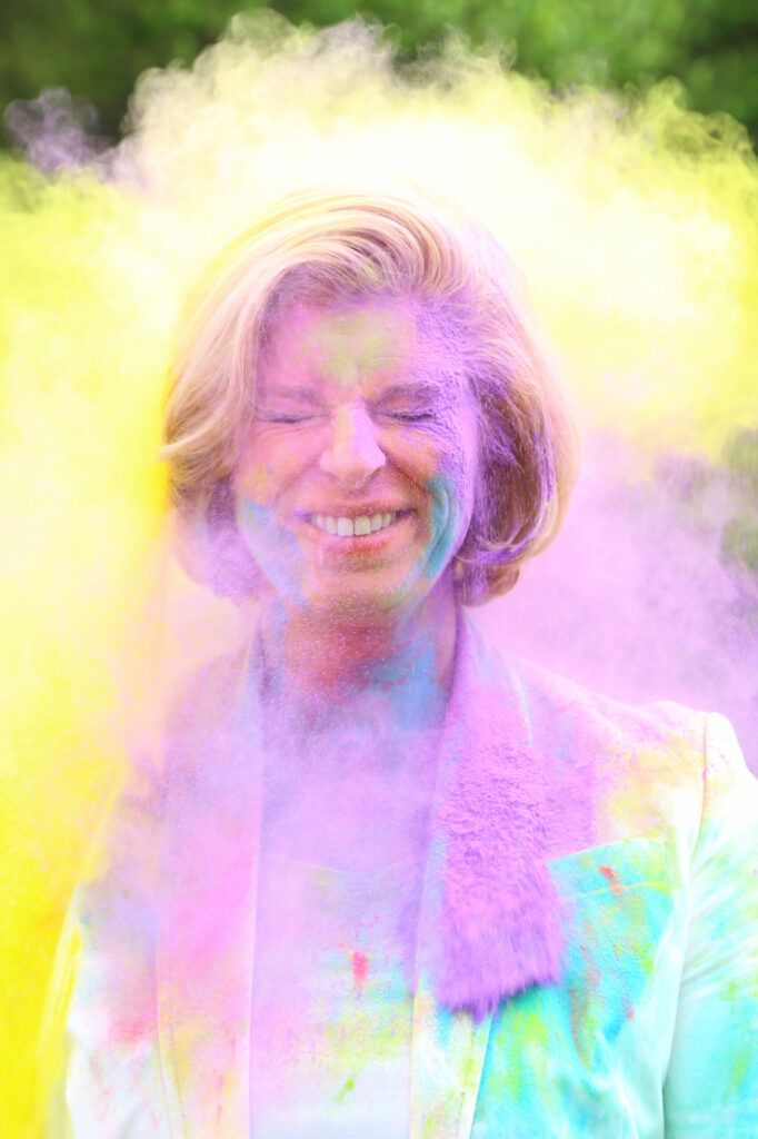 Vrouw onder het roze en gele poeder lacht naar de camera, ColorPowder-shoot