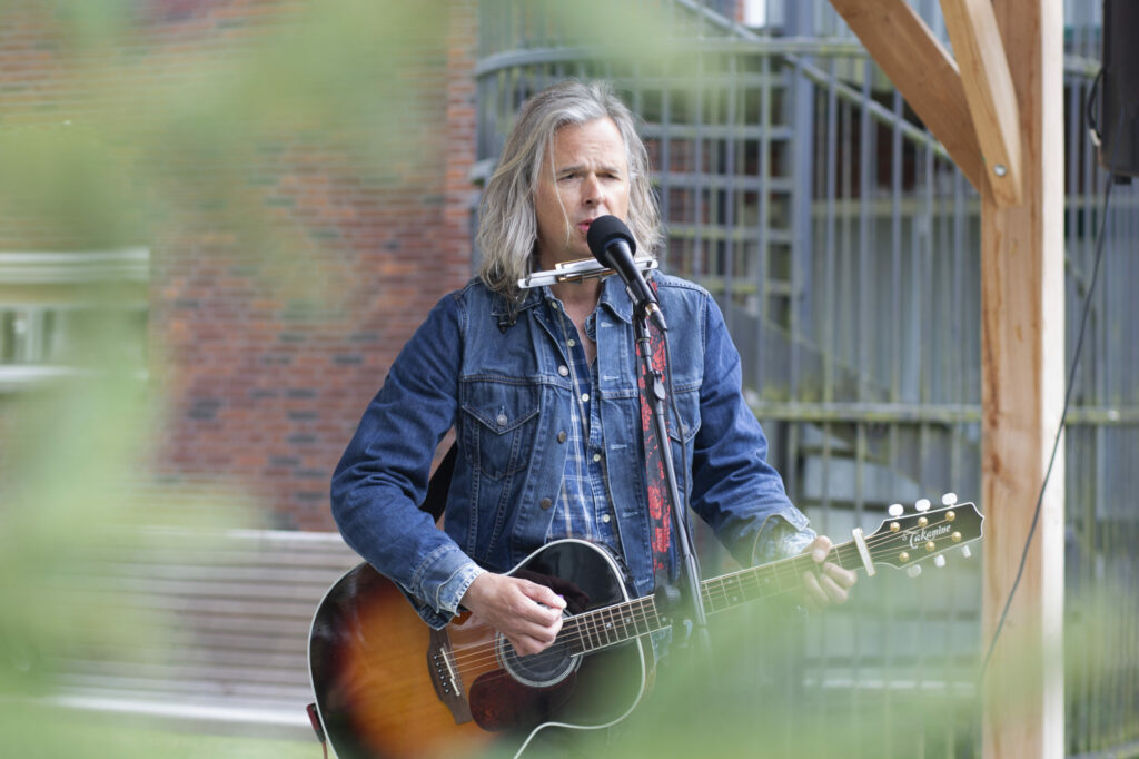 Zanger met gitaar treedt buiten op in spijkerjas, evenementfotografie