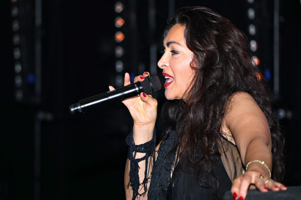 Zangeres met microfoon en lange donkere krullen tijdens een optreden
