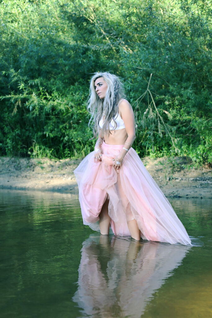 Vrouw in roze tuljurk staat in het water, fashion shoot buiten