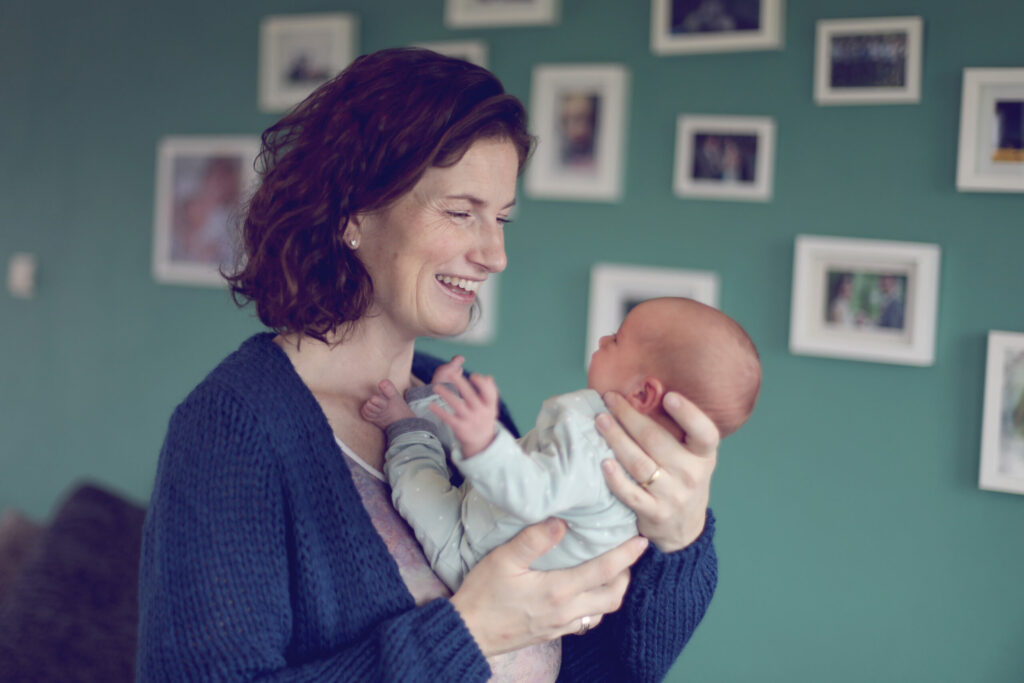 Vrouw met pasgeboren baby in haar armen voor een fotomuur, lifestylefoto
