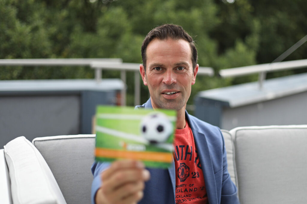 Man toont een voetbalkaart op een terras, portret voor een campagne