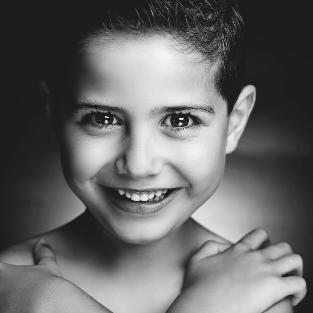 Zwart-witportret van een lachende jongen met de armen gekruist, Pure Portrait