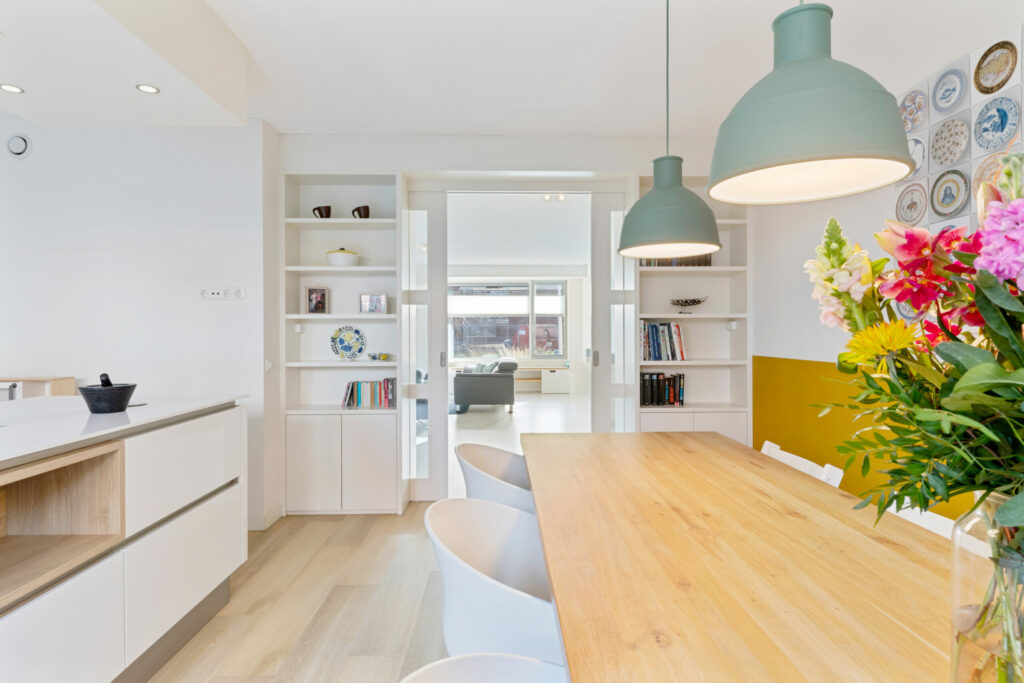 Lichte eethoek met houten tafel, bloemen en open keuken