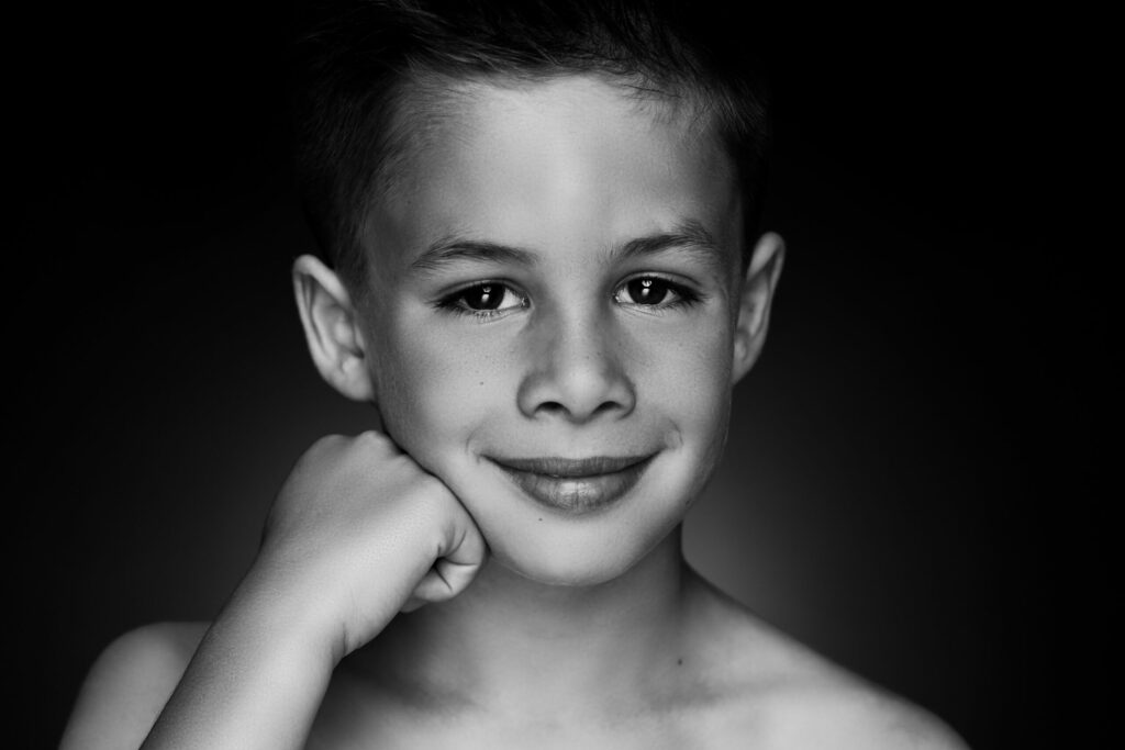 Zwart-witportret van een lachende jongen met de hand onder de kin