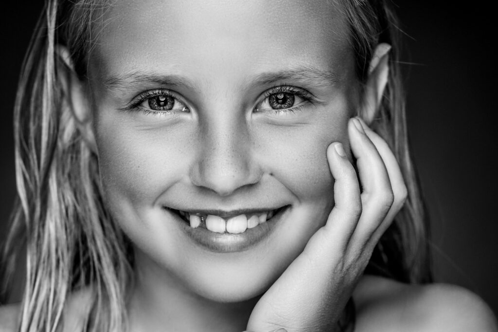 Zwart-witportret van een lachend meisje met de hand aan haar wang