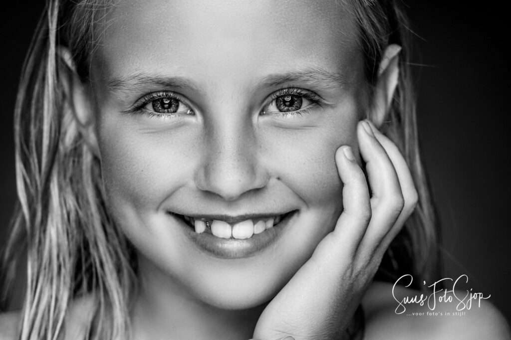 Zwart-witportret van een lachend meisje met de hand onder haar kin