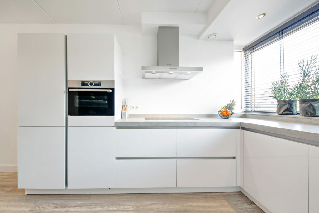 Witte keuken met inbouwapparatuur en groot raam, woningfoto